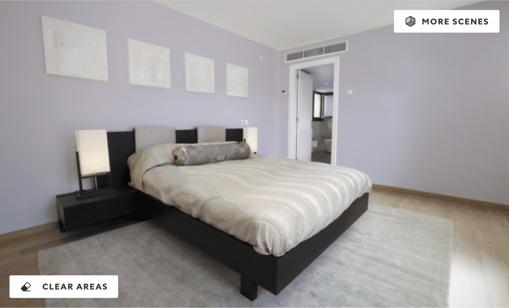 A modern bedroom featuring soft Inspired Lilac walls, neutral bedding, and minimalist decor. The room includes a low-profile bed, black side tables with lamps, and blank picture frames above the bed, with natural light coming from an adjoining bathroom.