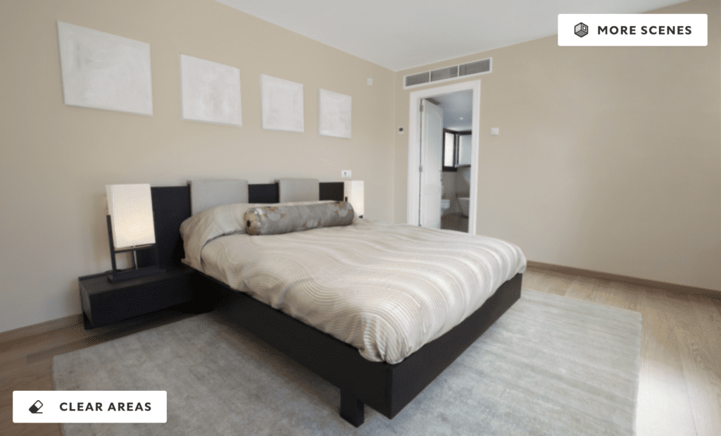 A modern bedroom with soft Navajo white walls, neutral bedding, and minimalistic decor. The room features a low-profile bed, two black side tables with lamps, and blank picture frames above the bed, with natural light coming from an adjoining bathroom.