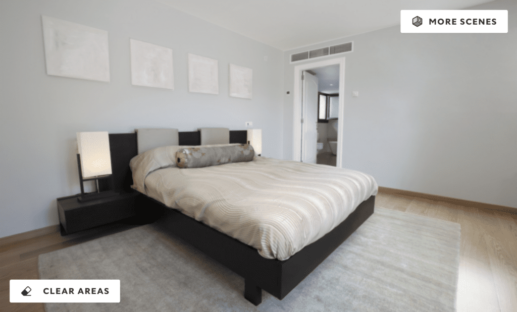 A modern bedroom with soft Winsome gray walls, neutral bedding, and minimalist decor. The room features a low-profile bed, black side tables with lamps, and blank picture frames above the bed, illuminated by natural light from an adjoining bathroom.